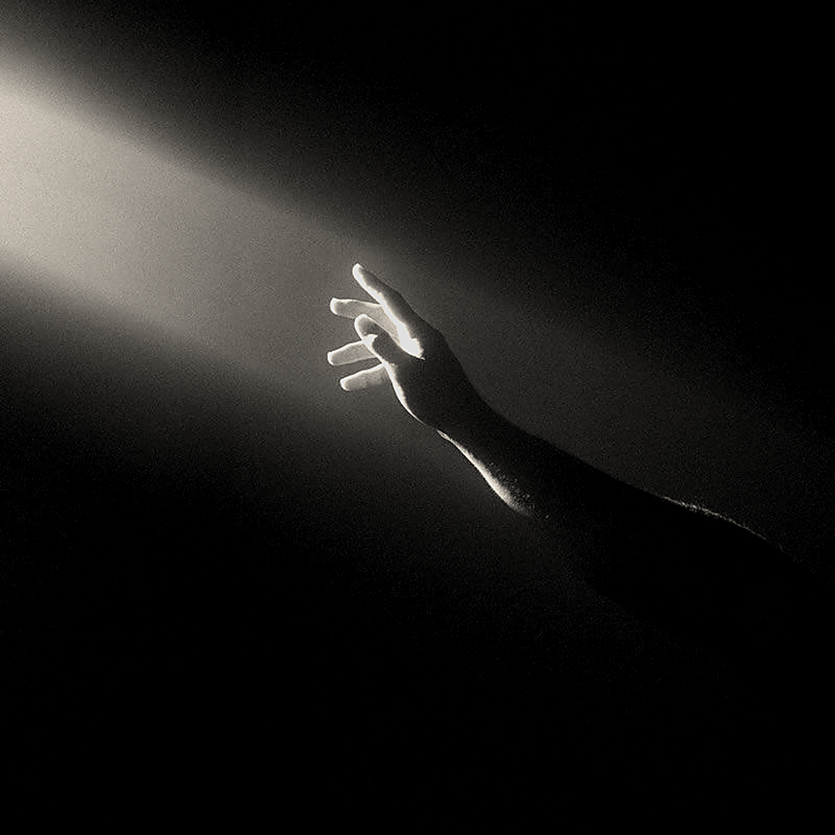 A hand reaches toward a thin beam of light in darkness.